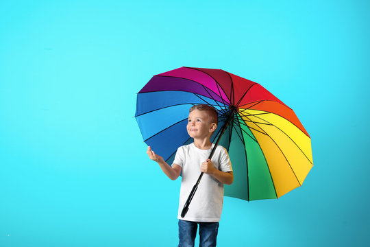Little boy with rainbow umbrella on color background