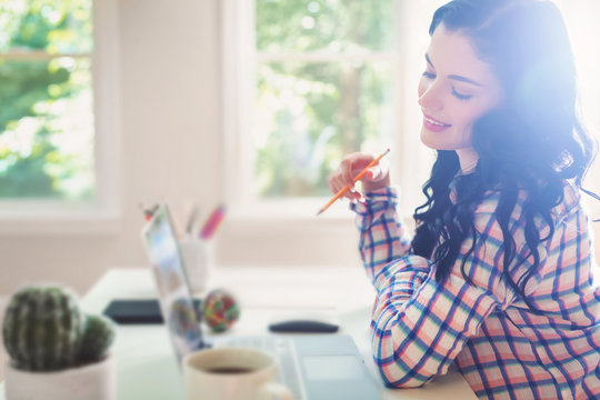 Young woman holding a pencil in frot of her laptop