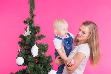 Holidays, family and christmas concept - young mom with her little daughter near christmas tree on pink background