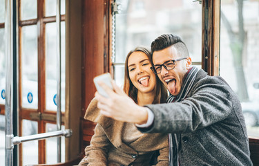 Happy young couple taking photos using mobile smart phone camera inside bus - Travel lovers making...