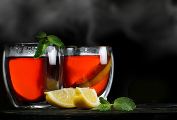 Hot tea in transparent glasses on a black background with mint and lemon, steam over cups