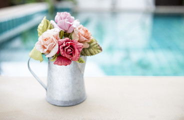 Beautiful rose paper flower in metal pot over blurred swimming pool background, outdoor day light