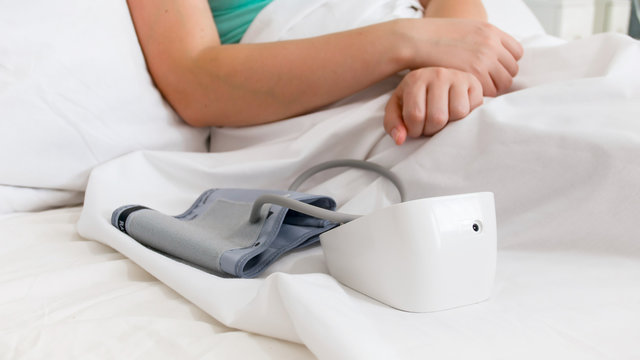 Closeup image of digital blood pressure monitor in bed of sick woman at hospital