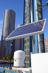 Solar panel in urban environment with buildings and skyscrapers in background with blue sky - 225186099