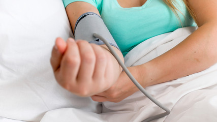 Closeup image of sick woman lying in bed and measuring blood pressure