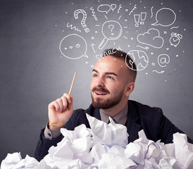 Young businessman sitting behind crumpled paper with mixed doodles over his head