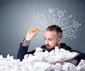 Young businessman sitting behind crumpled paper with drawings of gears and steam over his head