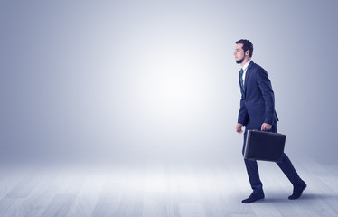 Obraz premium Successful businessman walking in front of an empty wall with briefcase on his hand 