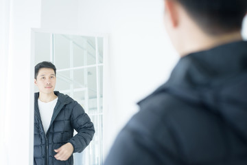 Asian handsome man looking at himself in mirror indoors