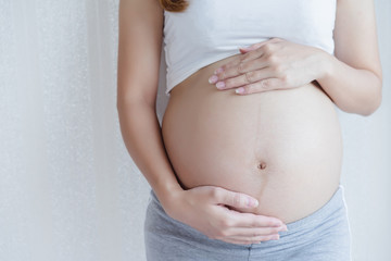 Attractive pregnant woman is standing and holding her belly. Last months of pregnancy.