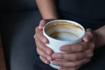 Closeup image of a woman's hands holding a white cup of hot coffee