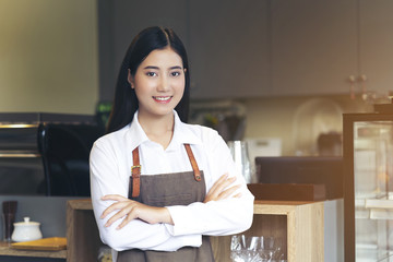 Portrait of young woman barista with brown apron uniform. Standing with arm cross pose, look professional of entrepreneur, beautiful female SME business ownership