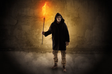 Ugly wayfarer with burning torch in his hand in front of a crumbly wall concept
