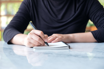 Closeup image of a woman writing on blank notebook on table with green nature background