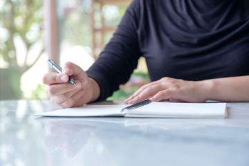 Closeup image of a woman writing on blank notebook on table with green nature background