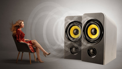 Stylish young lady sitting in a sofa and listening to big loudspeakers
