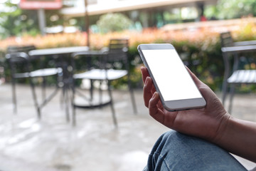 Mockup image of woman's hands holding white mobile phone with blank desktop screen while sitting in cafe