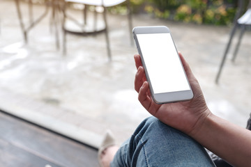Mockup image of woman's hands holding white mobile phone with blank desktop screen while sitting in cafe