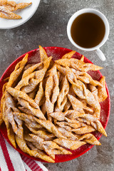 Crispy deep-fried angel wing or bowtie cookies sprinkled with powdered sugar, traditional biscuits in many European countries, photographed overhead (Selective Focus on the upper cookies)