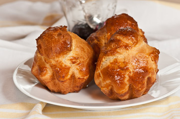 Top view, close distance of three freshly baked, brioche a tete, muffins on a round, white plate on a yellow and white cloth