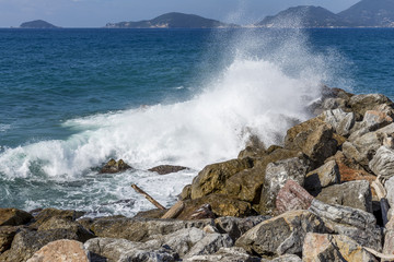 The waves of the sea break on the rocks of Tellaro, with the Gulf of La Spezia in the background, Liguria, Italy