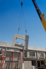 Construction site crane is lifting a precast concrete wall panel.