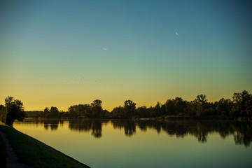 Airplanes leave contrails against the blue sky during the golden hour at sunset over the Inn river