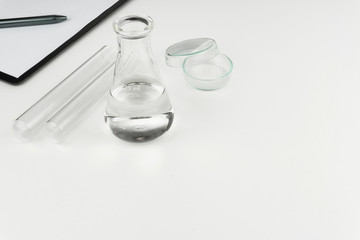 laboratory equipments. A clear liquid flask, test tubes, petri dish and a clipboard with pen on the...