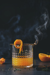 Glass of Scotch Whiskey orange juice alcohol cocktail with swirled orange peel on skewer, thyme and...