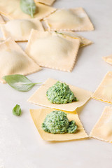 Homemade raw uncooked italian pasta ravioli staffed by spinach ricotta over white marble background. Close up, space