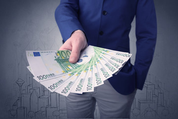 Young businessman holding large amount of bills with grungy drawings of a city and numbers behind...