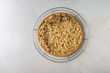 Homemade sweet apple walnut shortbread tart on cooling rack over white marble background. Autumn baking. Flat lay, space