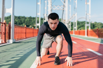 Portrait of professional runner at start ready to sprint. Sports man listening music using wireless...