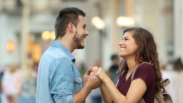 Side view of a happy couple flirting holding hands in the street