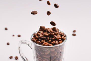 Grains of coffee are poured into a glass cup on a white background