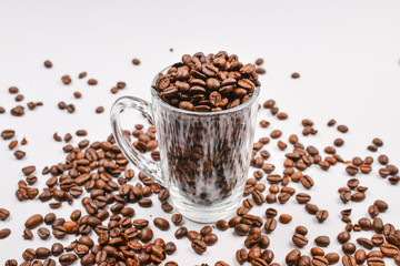 Grains of coffee are poured into a glass cup on a white background