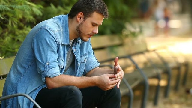 Closeup of a sad husband complaining after divorce holding the wedding ring in a park