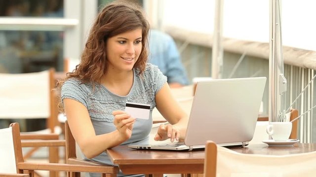 Happy woman shopping with a laptop and paying with credit card in a coffee shop