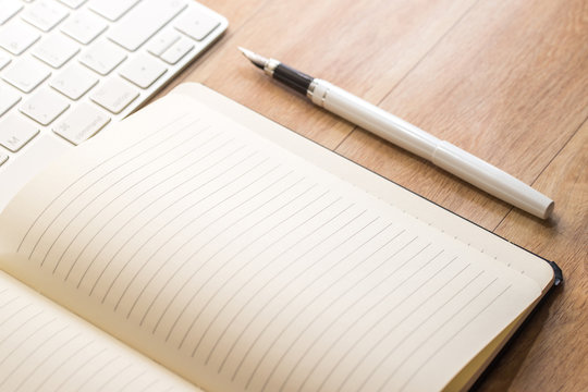 Office table with notepad, keyboard and fountain pen. View from above