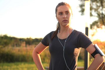 Young attractive sporty fitness woman standing outdoors at sunset or sunrise in city.