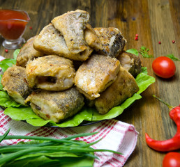 fried fish pike pieces on a plate on a wooden table next to tomatoes and greens 