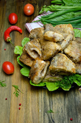 fried fish pike pieces on a plate on a wooden table next to tomatoes and greens 