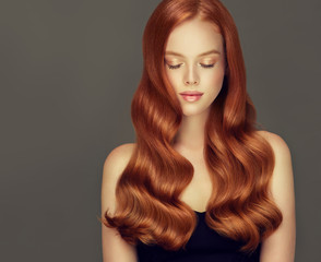 Red head girl with long  and   shiny curly hair .  Beautiful  model woman  with wavy  hairstyle. Care , cosmetic and beauty products

