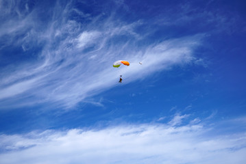 Lighty color tandem parachute against the background of great clouds and silhouettes of skydivers