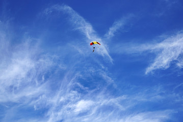 Bright multicolor parachute canopy and skydivers silhouettes against the background of a blue sky