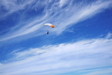 White parachute canopy against the background of unusual clouds and silhouettes of tandem's skydivers