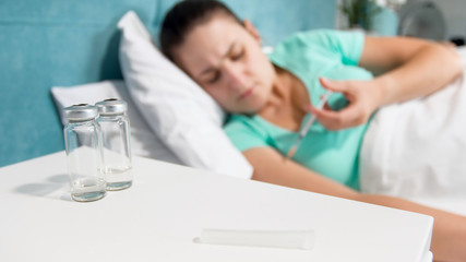 Out of focus image of sick woman lying in bed and making herself injection with syringe