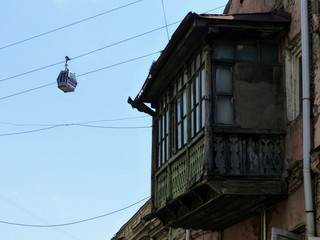 Fototapeta na wymiar Cabina di un funicolare nel cielo con in primo piano un vecchio balcone coperto a Tbilissi in Georgia.