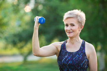 stylish elderly woman with short hairstyle doing sports with dumbbells in summer in the park