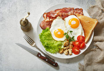 breakfast with plate of fried eggs, bacon, mushrooms and toast
